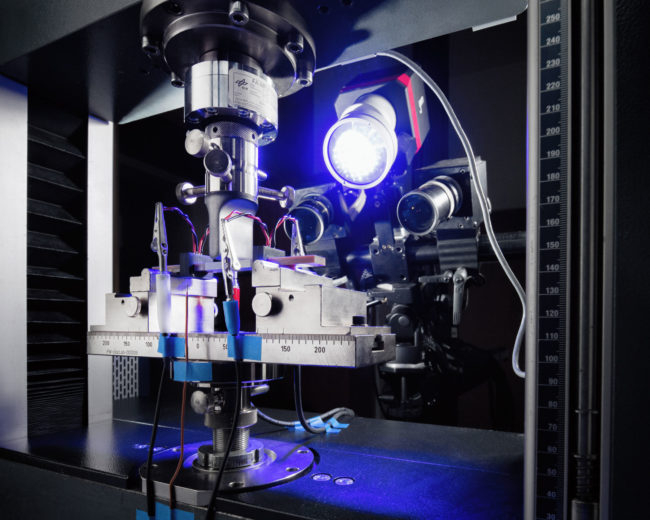 Glasfaserverstärkte Kunststoffprobe im Biegeversuch. Der Superkondensator ist mittig im Randbereich der Probe integriert. Die mechanische Messung wird durch eine elektrochemische Messung begleitet.