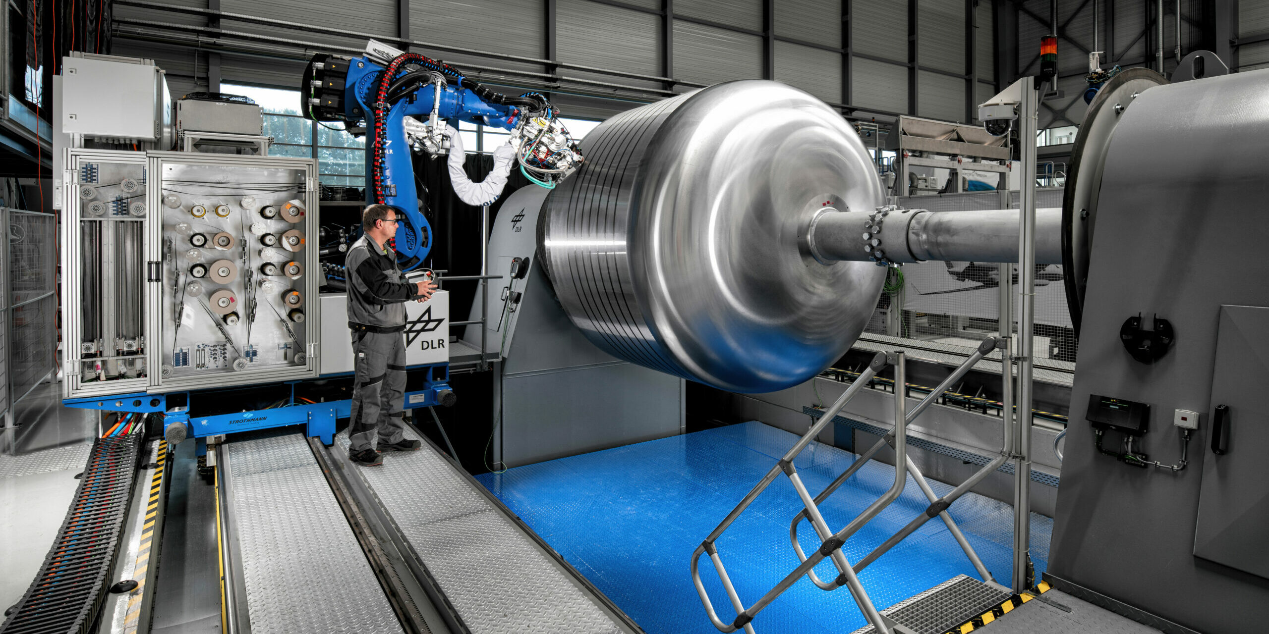 Hystor-(5)_Web Zeigt dir GroFi-Anlage mit einem Roboterarm in betrieb. Dieser legt Tape auf dem Werkzeug für die Tankherstellung ab.