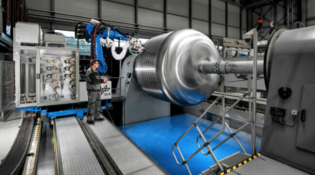 Hystor-(5)_Web Zeigt dir GroFi-Anlage mit einem Roboterarm in betrieb. Dieser legt Tape auf dem Werkzeug für die Tankherstellung ab.